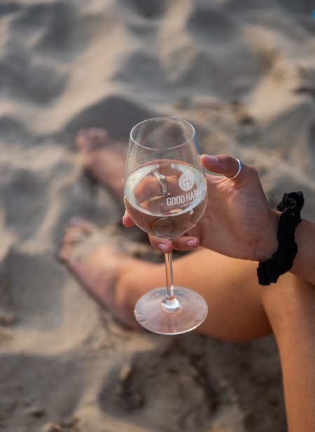 A woman sitting on a beach in Lake Leelanau, MI, holding a glass of Good Harbor wine